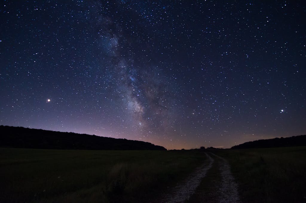 A stunning view of the Milky Way dominating the night sky over a serene open field pathway.